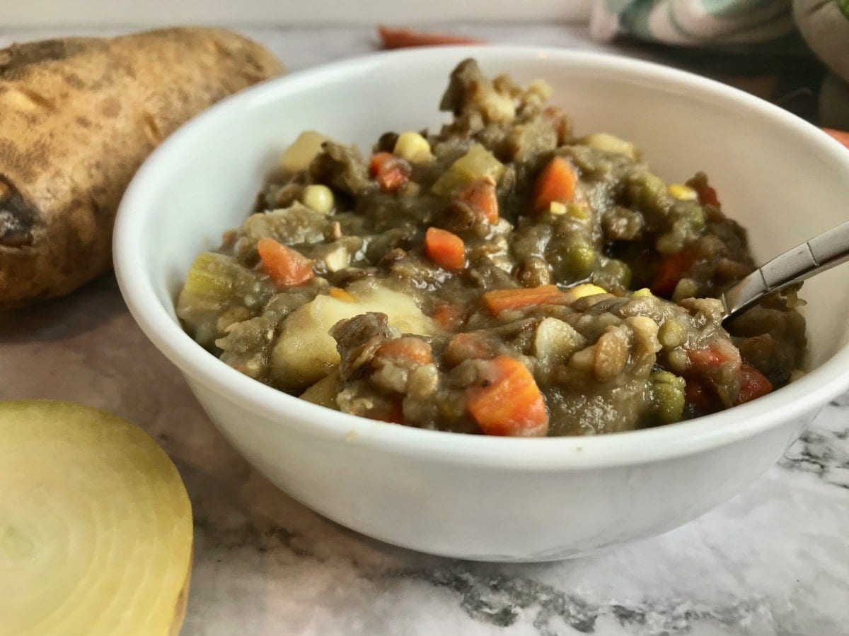 Vegan lentil stew in a bowl next to half an onion and a potato