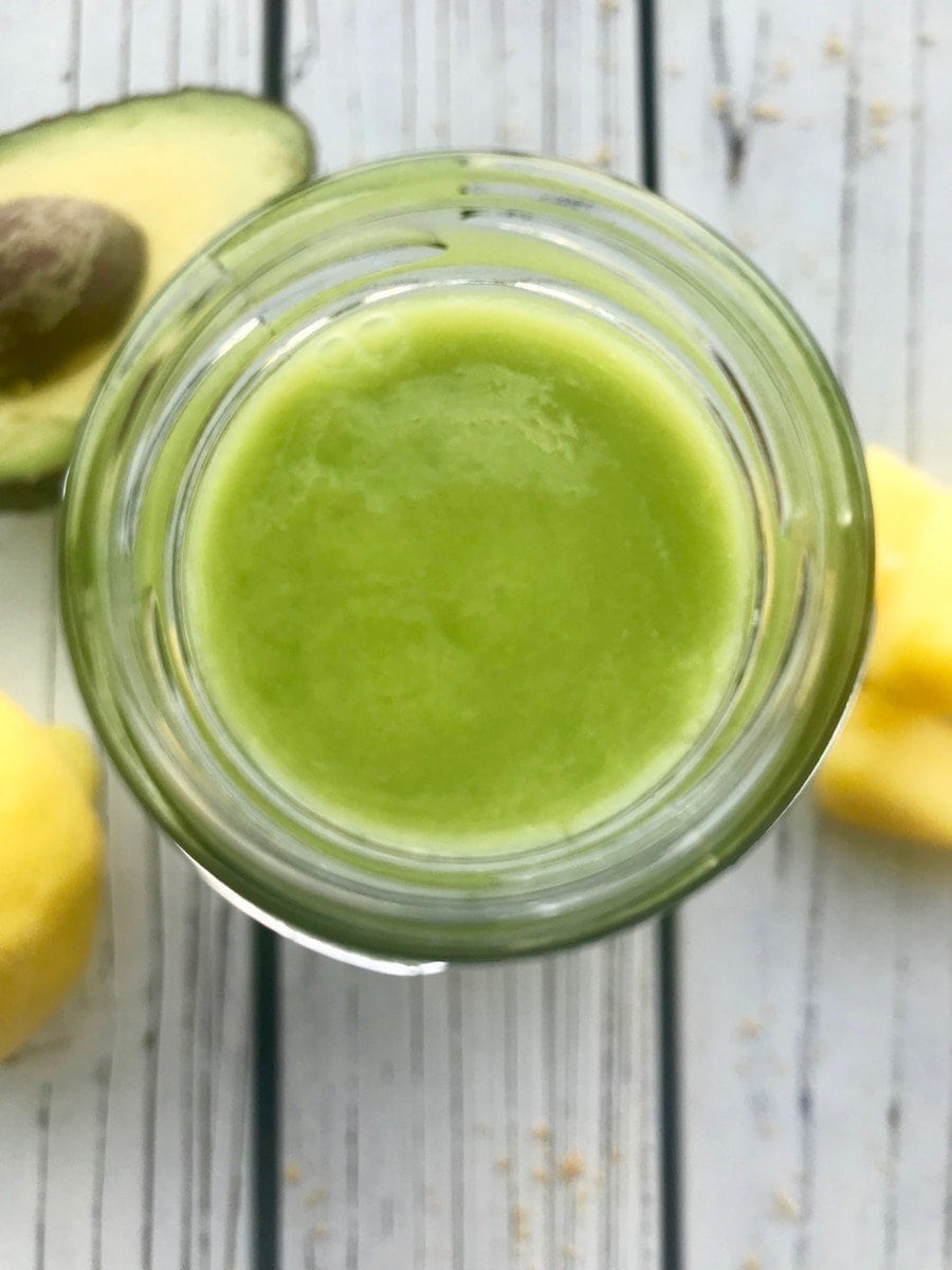 Overhead view of a green avocado smoothie in a glass bottle.