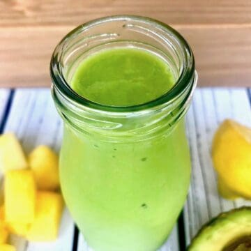 A green smoothie in a glass bottle, next to chopped pineapple and avocado.