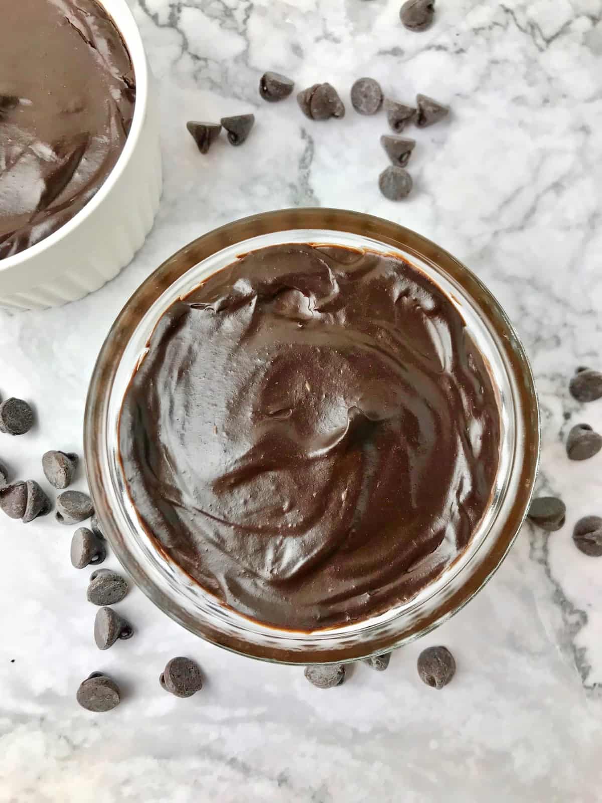 A bowl of avocado chocolate pudding next to some chocolate chips.