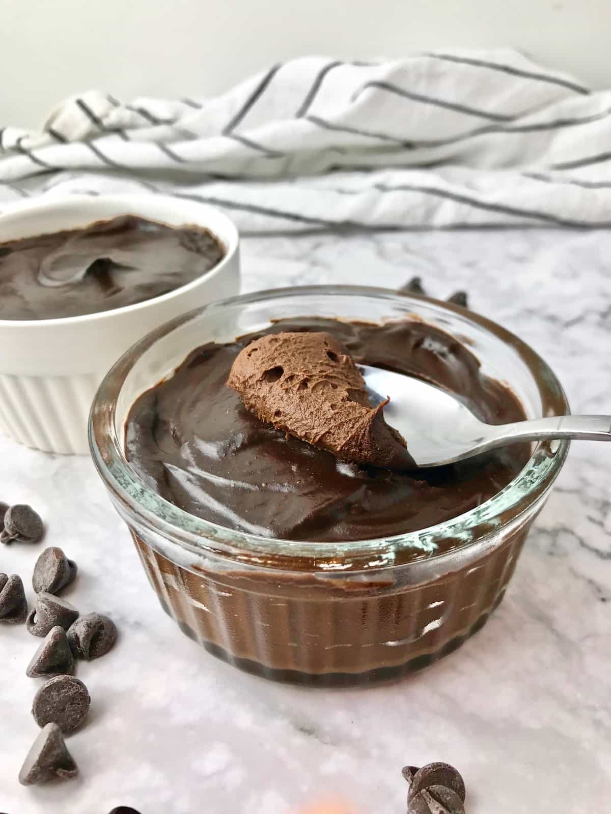 A bowl of chocolate mousse with a spoonful on top, next to some chocolate chips.