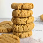 A stack of five peanut butter cookies next to two other peanut butter cookies on a table.