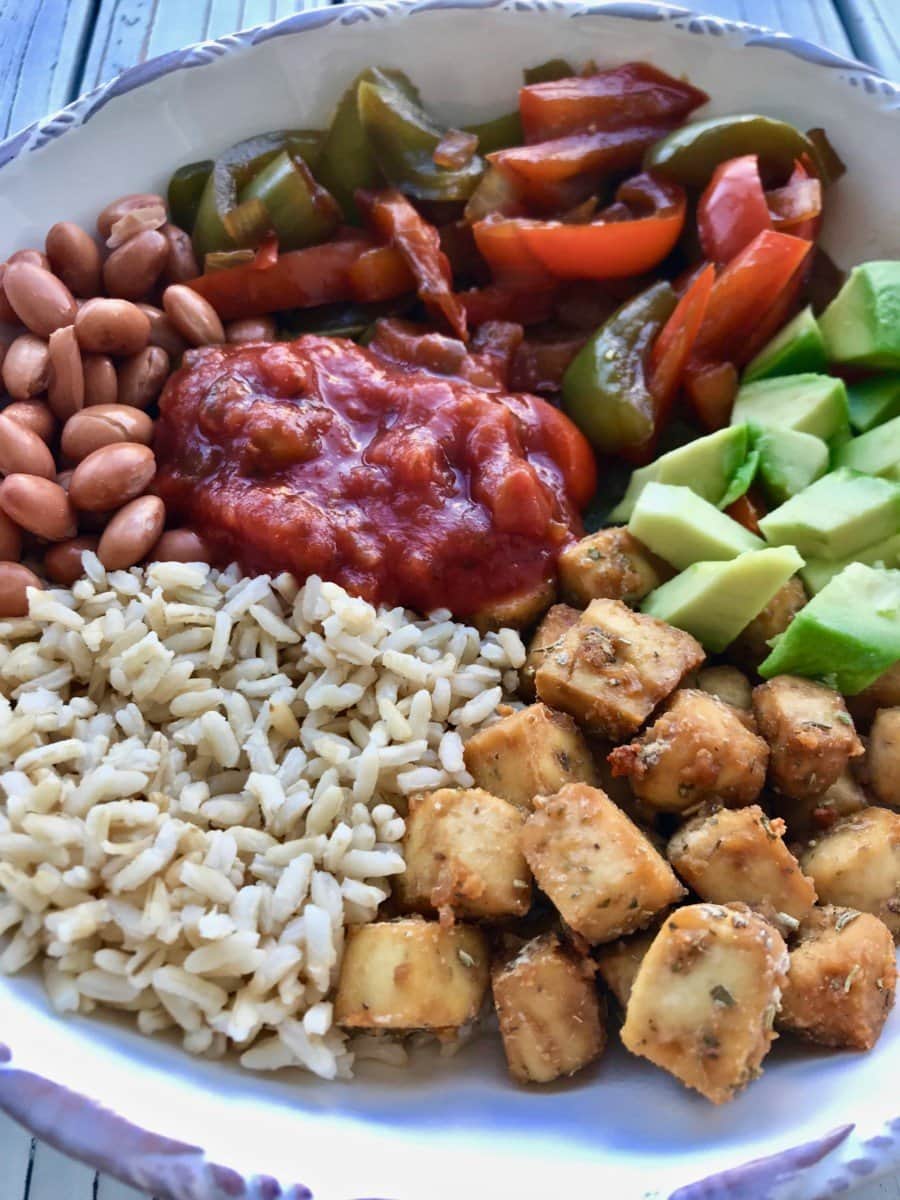 A bowl of rice, tofu cubes, avocado, beans, salsa, and cooked peppers.