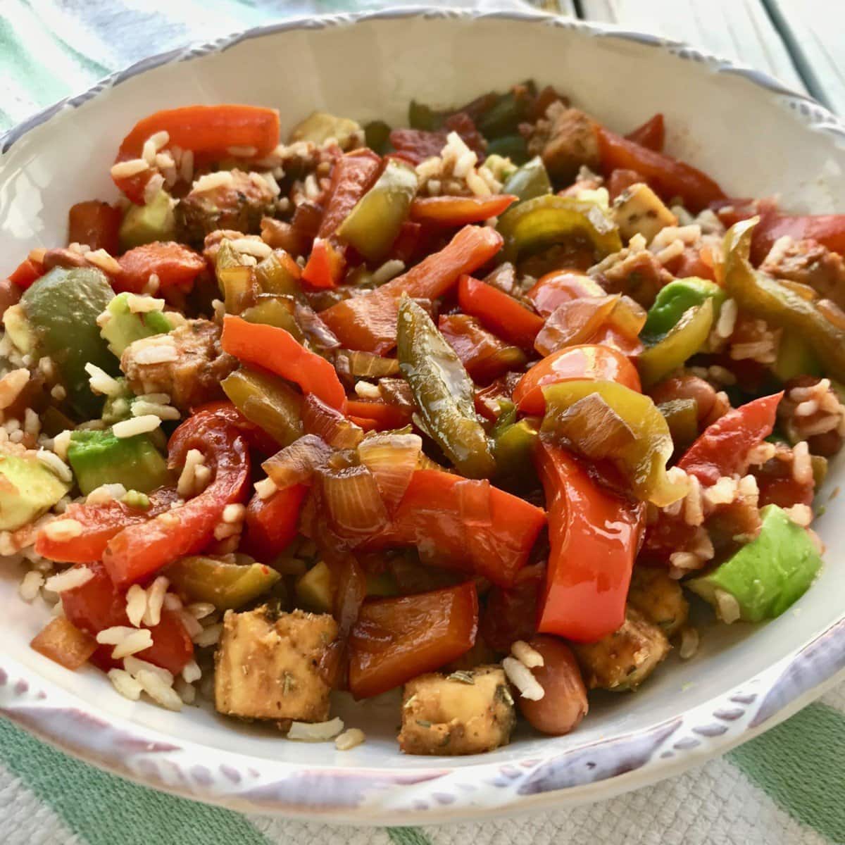 A bowl of peppers, rice, tofu, and onion.