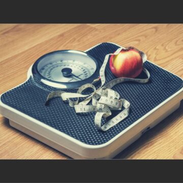 A weighing scale with an apple and a body measuring tape on it.