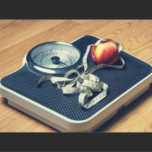 A weighing scale with an apple and a body measuring tape on it.