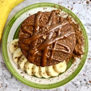 Overhead view of chocolate pancakes with chocolate syrup on top and banana slices on the plate.