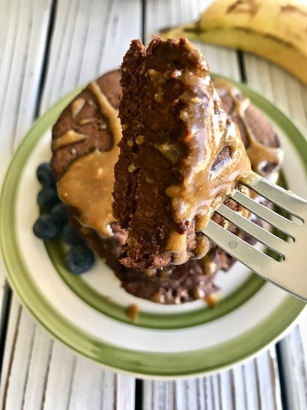 Close-up of a piece of chocolate banana pancakes on a fork with a stack of pancakes in the background.