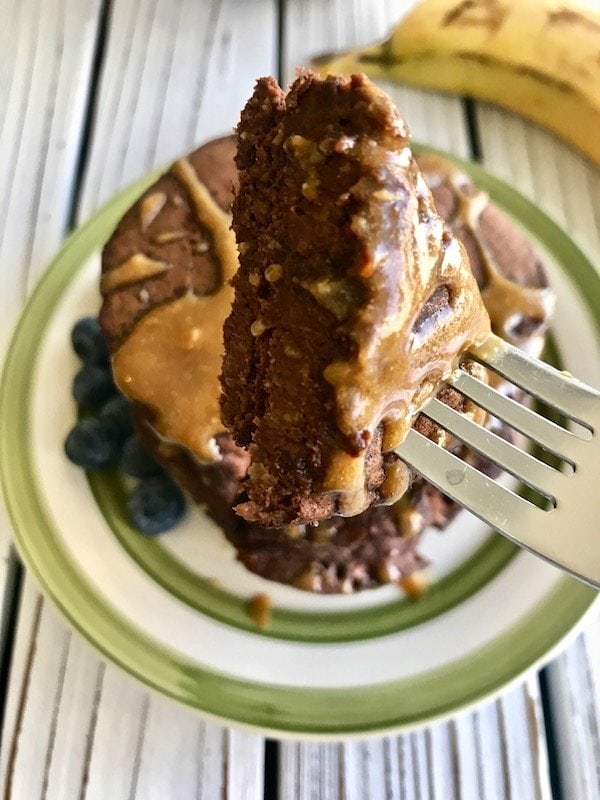 Close up of a piece of chocolate banana pancakes on a fork with a stack of pancakes in the background.