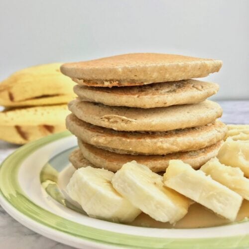 Stack of pancakes on a plate with banana slices in front of the stack.