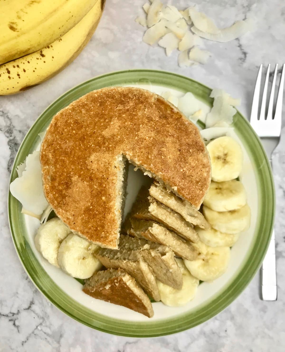 Overhead view of a stack of pancakes with a cut slice on a plate with sliced ​​bananas.