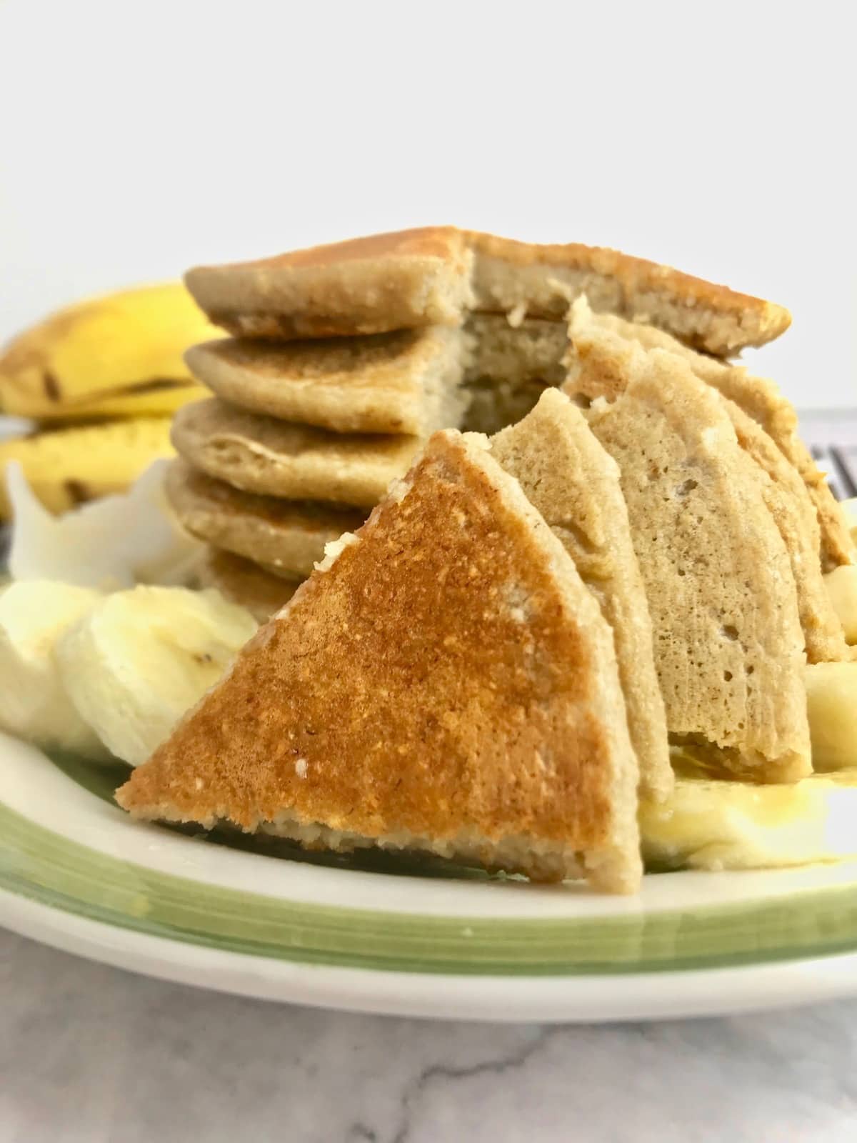 Triangle slices of pancakes in front of a stack of pancakes with bananas in the background.