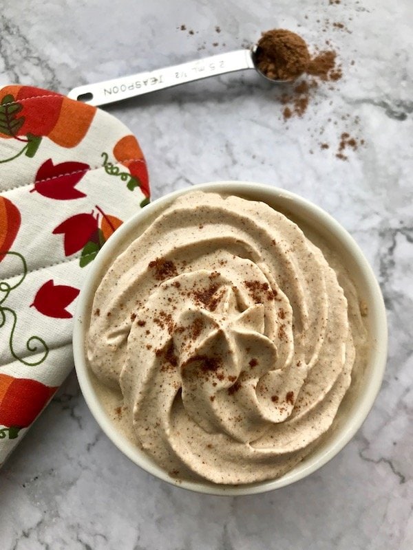 Small bowl of pumpkin whipped cream with some pumpkin pie spice on the table and an oven mitt. 