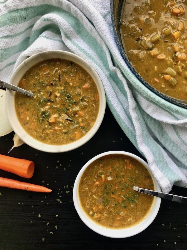 Two bowls of wild rice soup on a table with carrots.