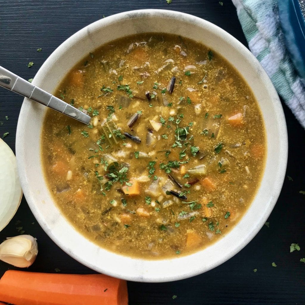 Vegan wild rice soup in a bowl with ingredients on the table.