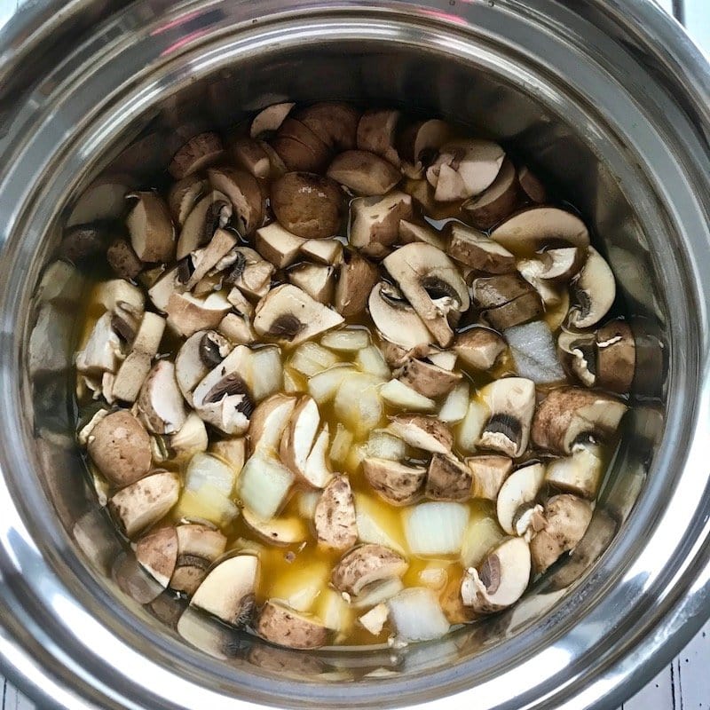 Chopped mushrooms and onion with vegetable broth in a pot. 