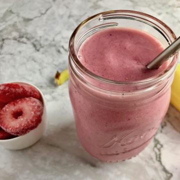 Pin strawberry banana raspberry smoothie in a mason jar with fruit on the table.