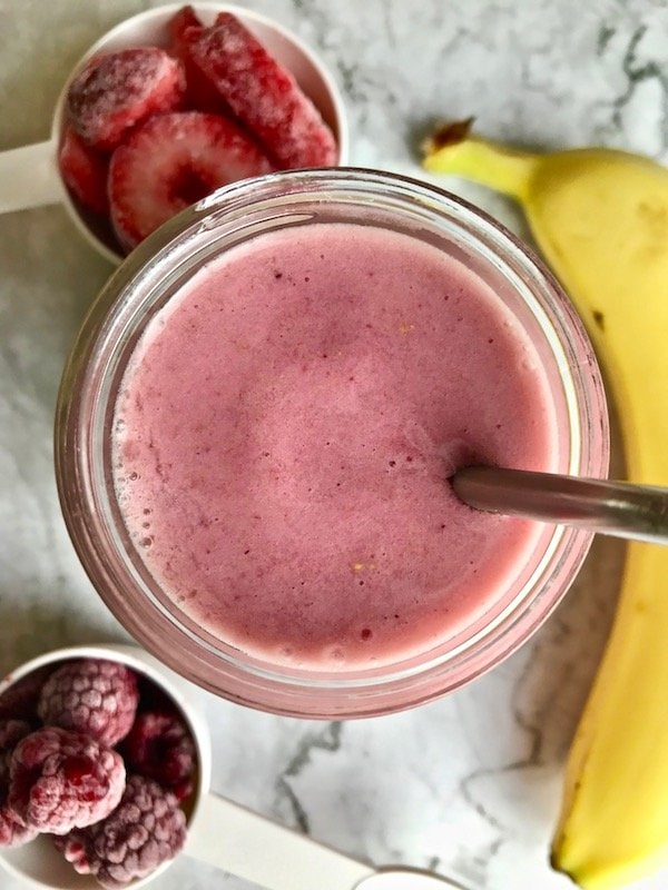 Close up of top of strawberry banana raspberry smoothie in a mason jar with ingredients in the background.