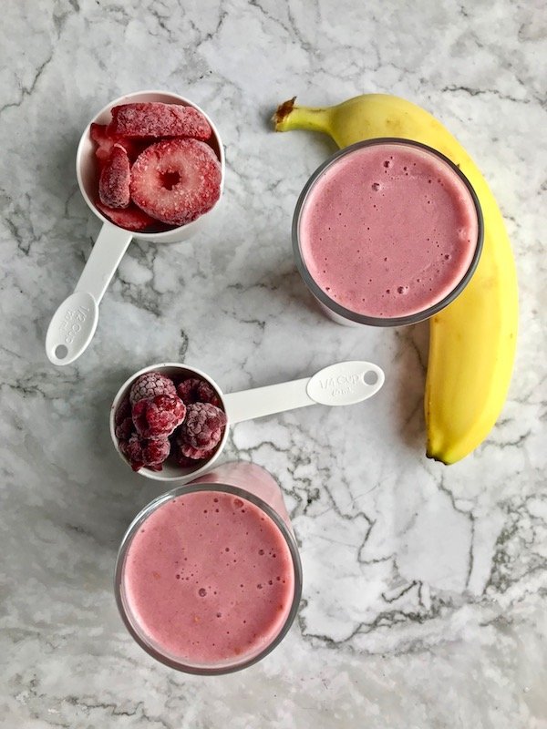 Two smoothies with banana, strawberries, and raspberries on the table. 