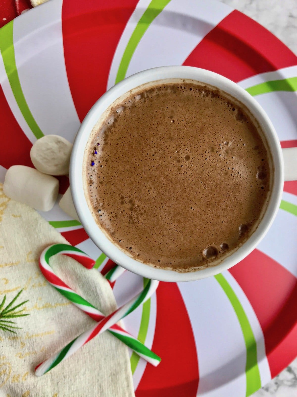 Cinnamon hot chocolate with oat milk sitting next to marshmallows and candy canes.