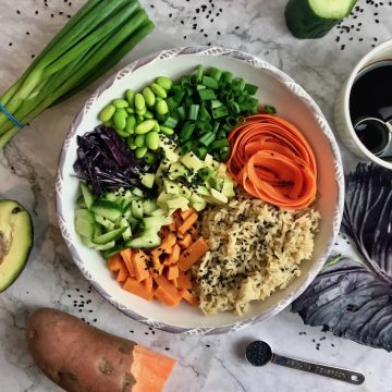 Vegan deconstructed sushi bowl, surrounded by ingredients: scallions, avocado, sweet potato, cucumber, red cabbage.