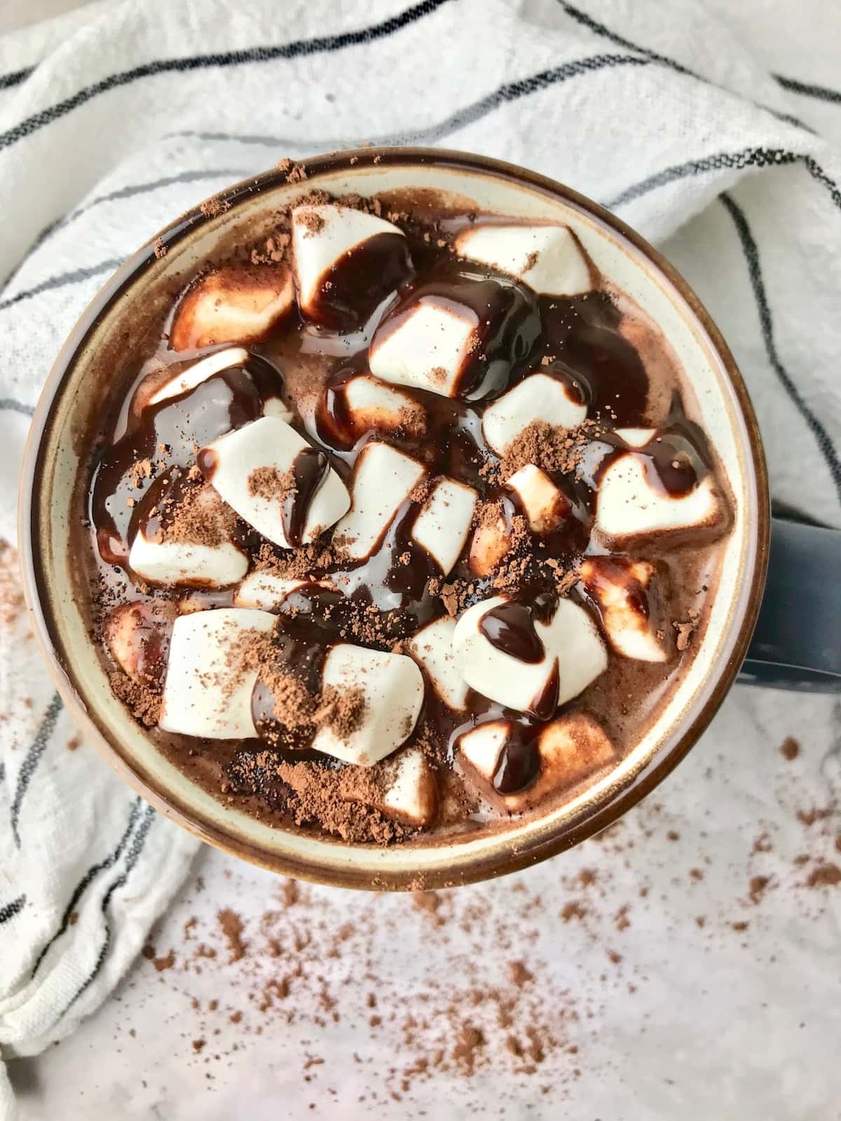 Overhead view of hot chocolate in a mug topped with marshmallows and chocolate sauce.