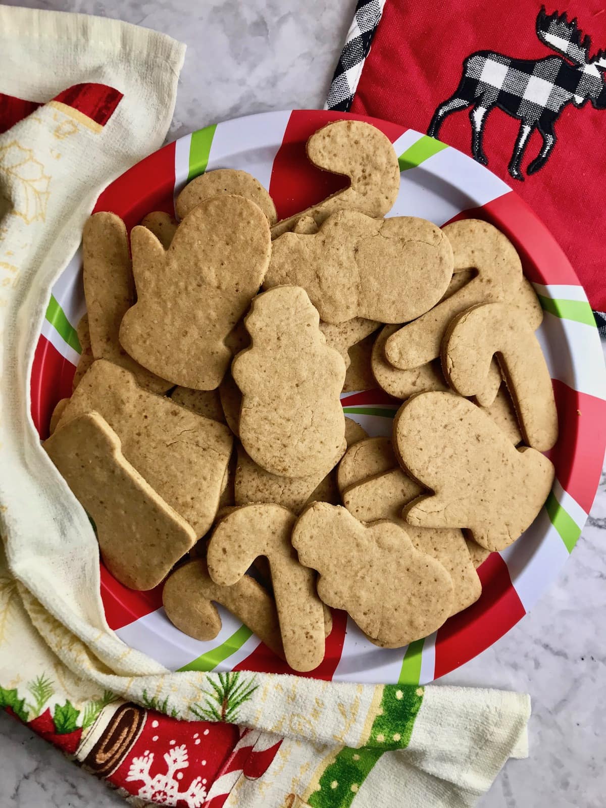 Plate full of Christmas-shaped cut-out cookies on a red, green, and white striped plate.