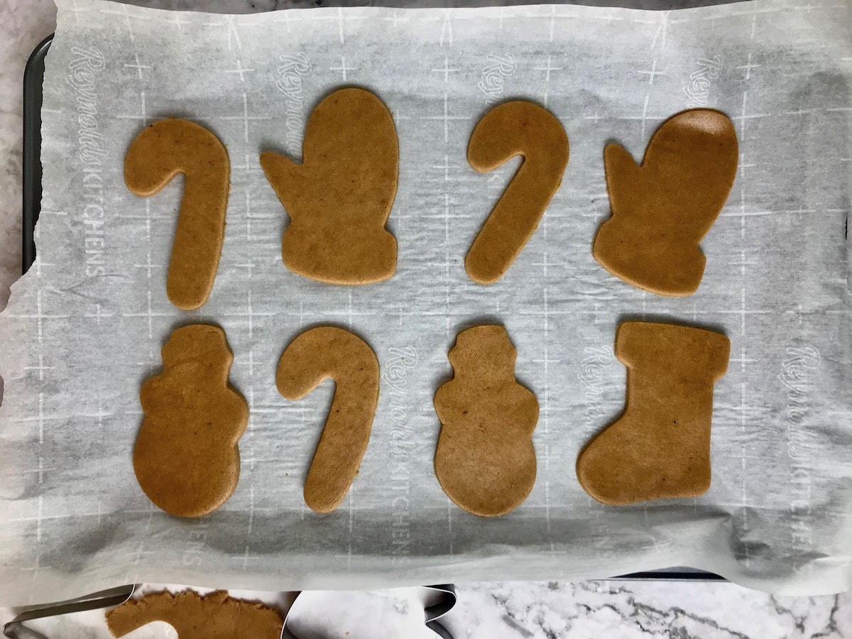Coconut sugar cookie dough in Christmas-shaped cut-outs on a baking sheet.