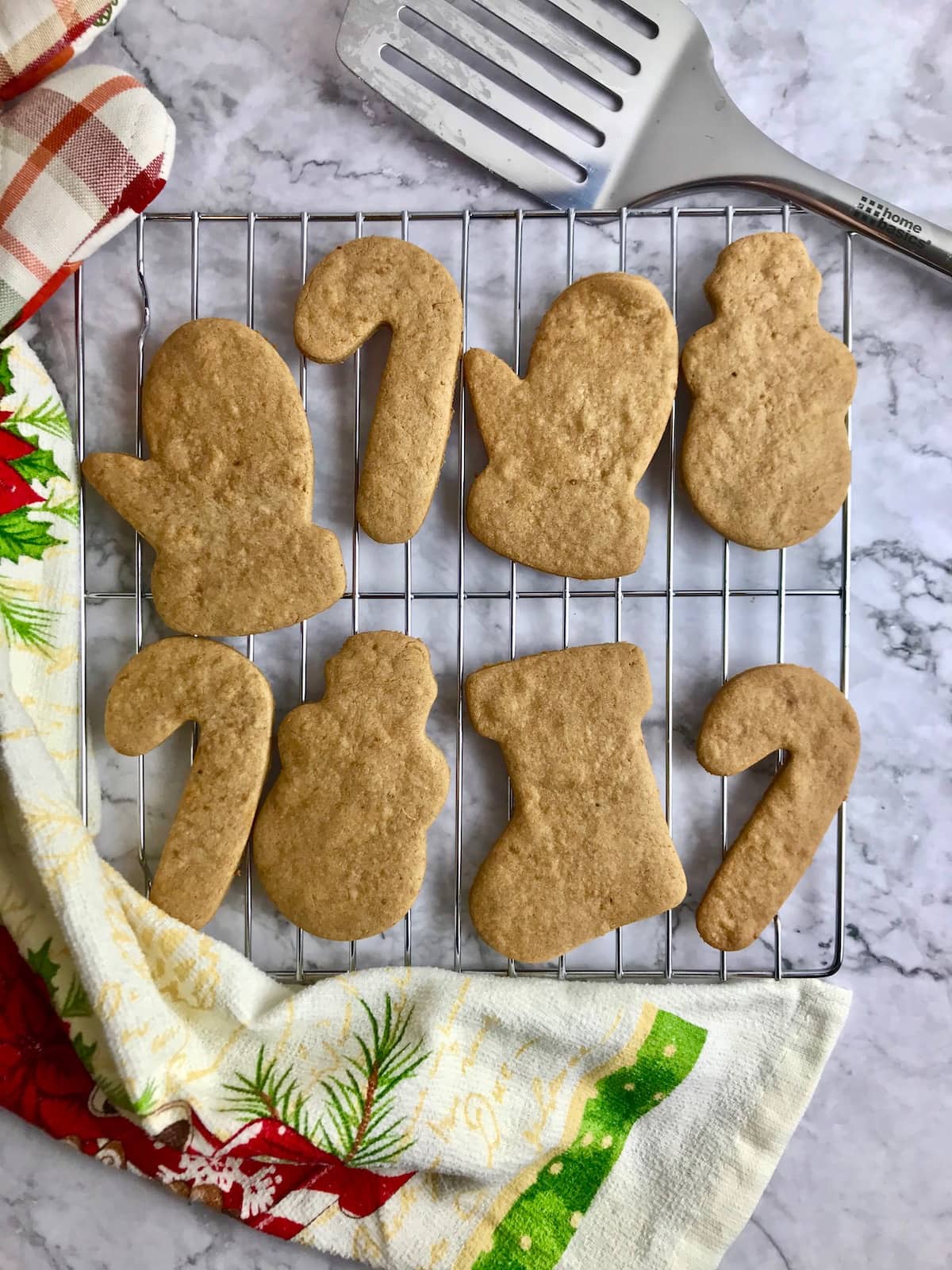 Vegan coconut sugar cookies with Christmas shapes on a cooling rack, next to a Christmas dish towel.