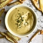 Vegan honey mustard dip surrounded by fries.