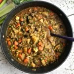 Large dutch oven filled with vegetable stew, with celery, carrot, and broccoli on the table.