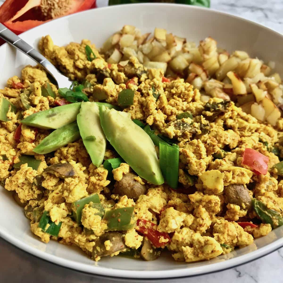 Oil-free tofu scramble topped with avocado and a side of potatoes.