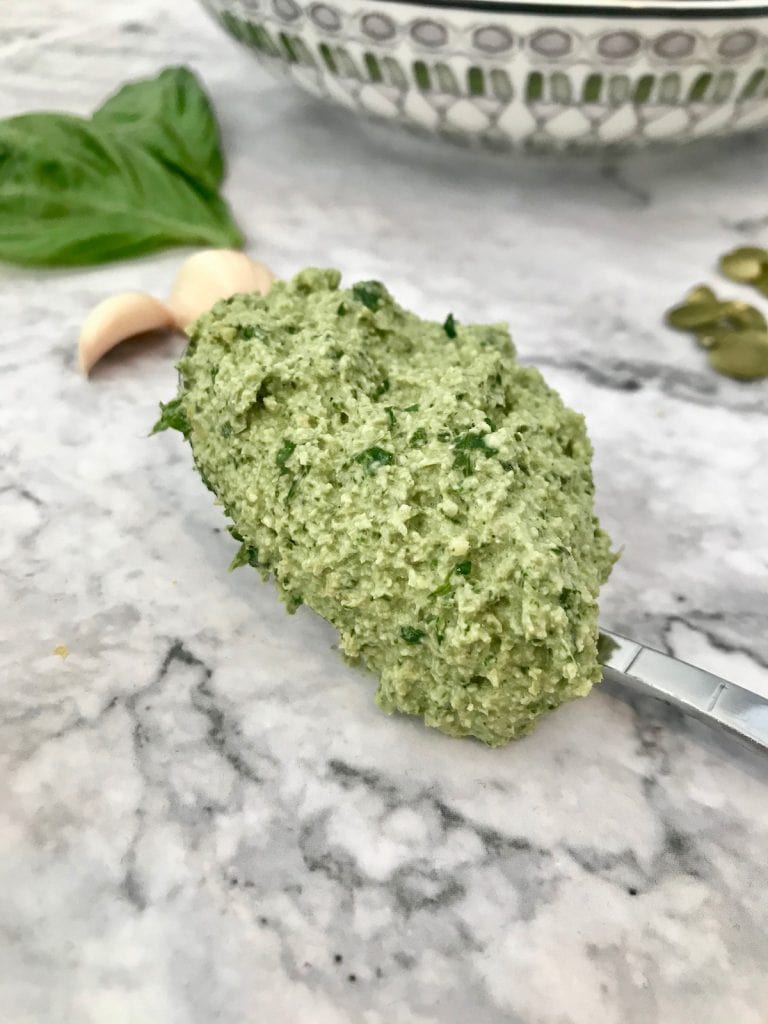 Thick green vegan pesto on a spoon, laying on a marble surface.