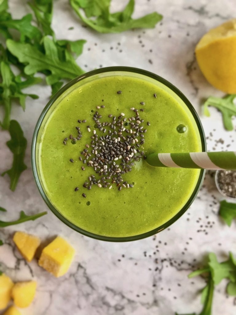 Overhead view of a green smoothie with chia seeds on top and ingredients in the background.