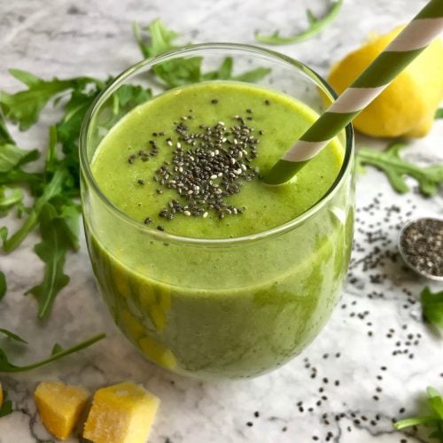 Green smoothie with chia seeds surrounded by arugula, pineapple, and lemon.