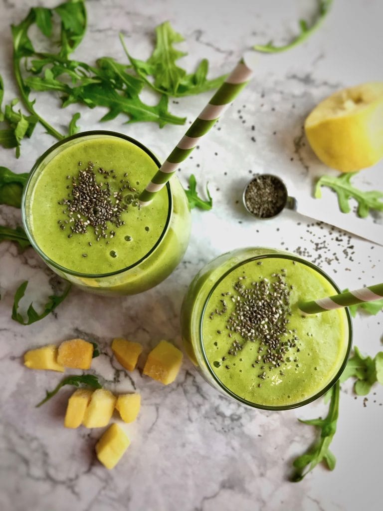 Overhead view on two green smoothies with chia seeds sprinkled on top. Smoothie ingredients are also on the table. 