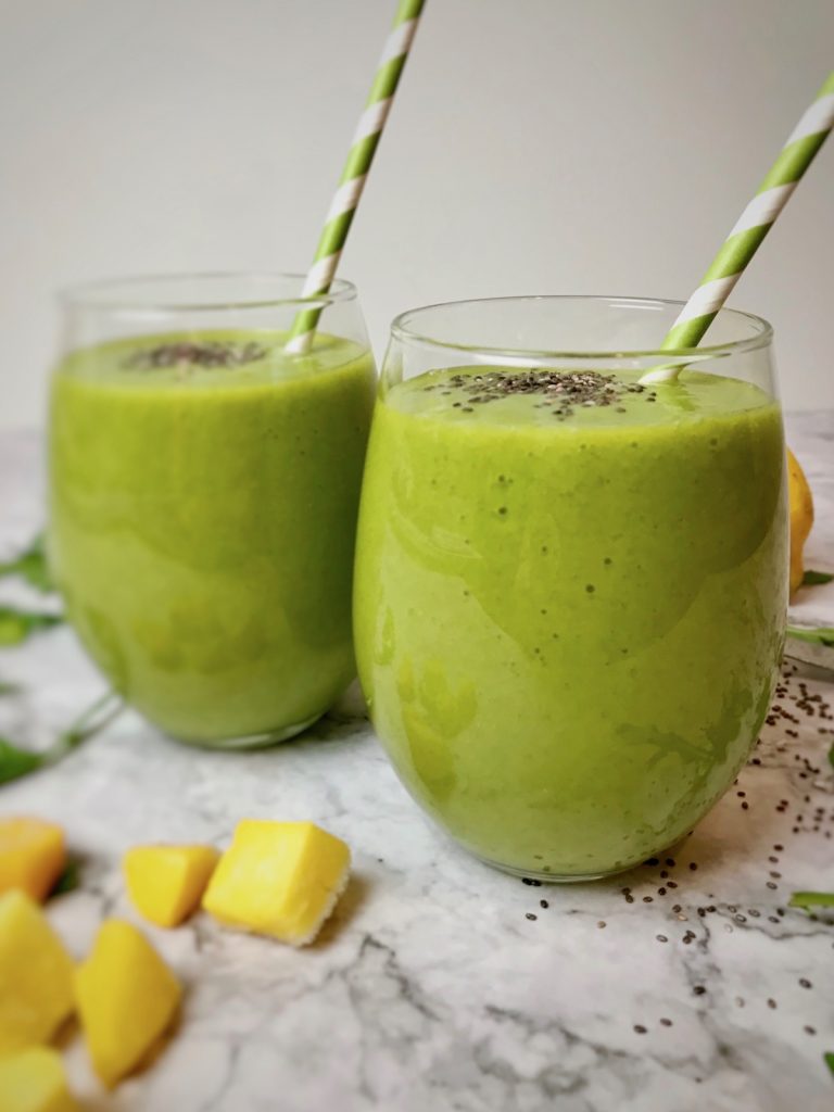 Two green smoothies in stemless wine glasses with green and white striped straws. 