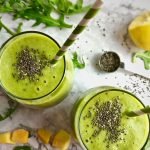 Two green smoothies topped with chia seeds and text that says Arugula Smoothie with Pineapple and Mango.