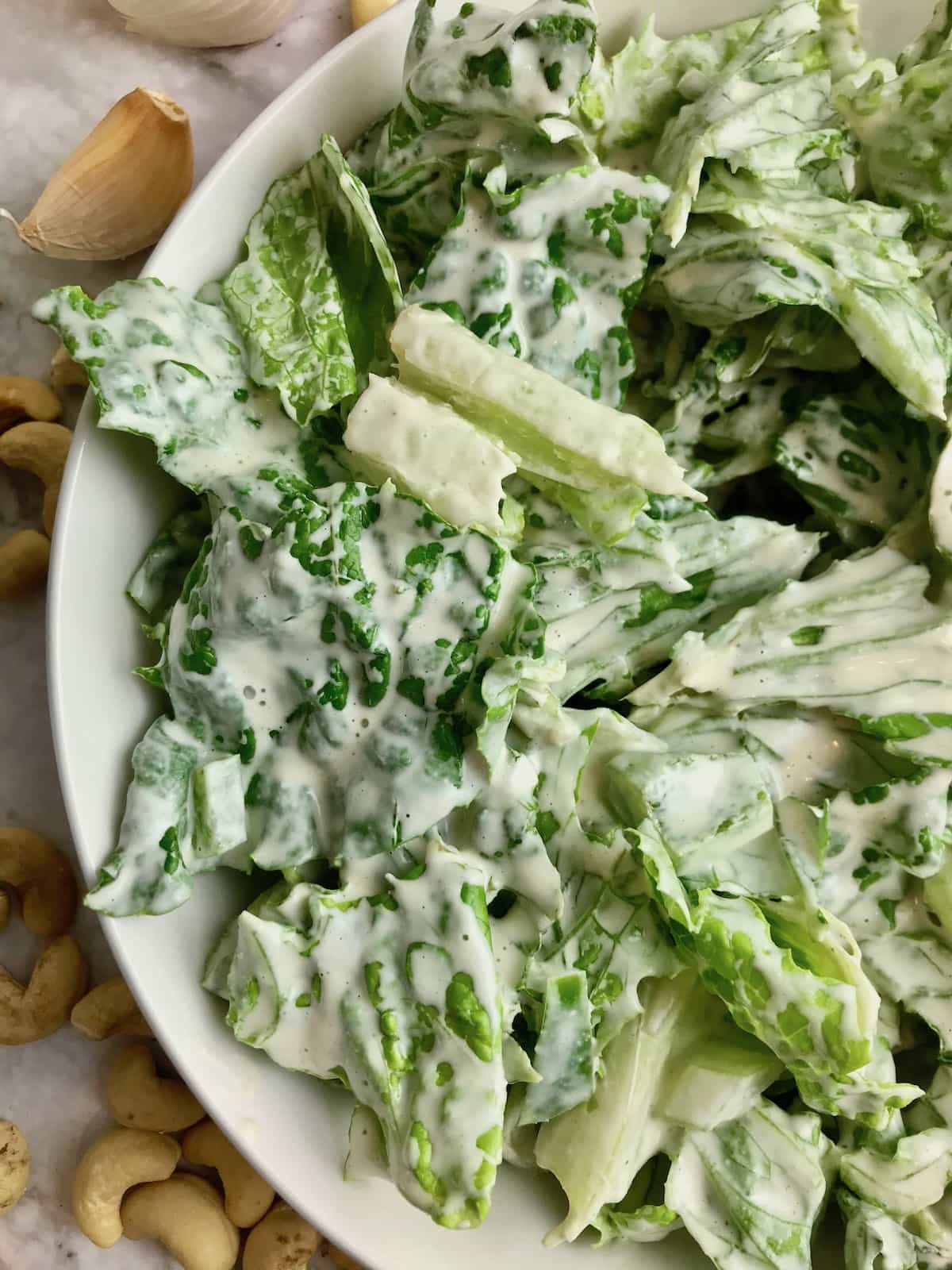 Close up of half a bowl of Romaine lettuce covered in white Caesar dressing. 