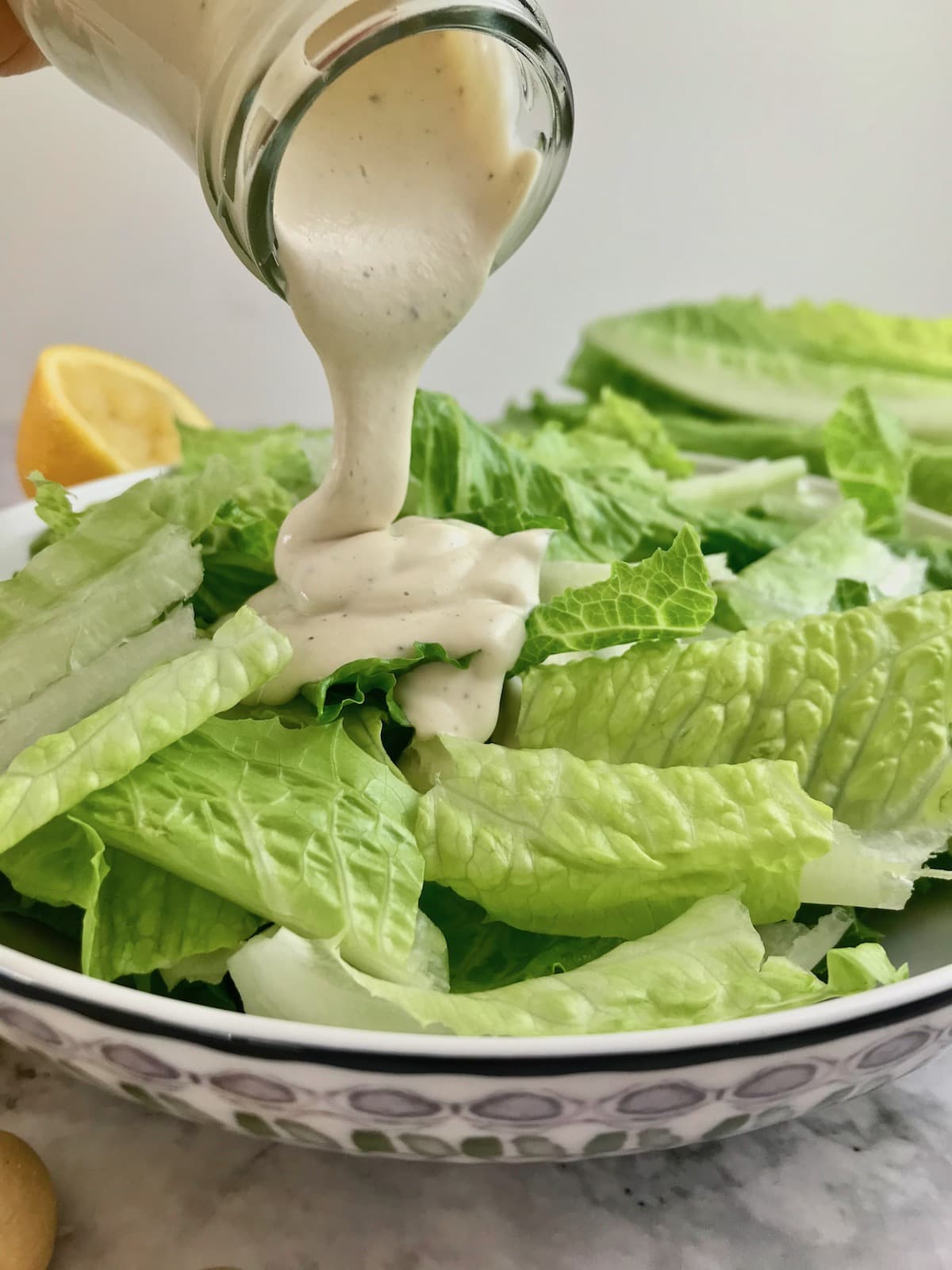 White Caesar dressing being poured onto a bowl or green romaine lettuce. 