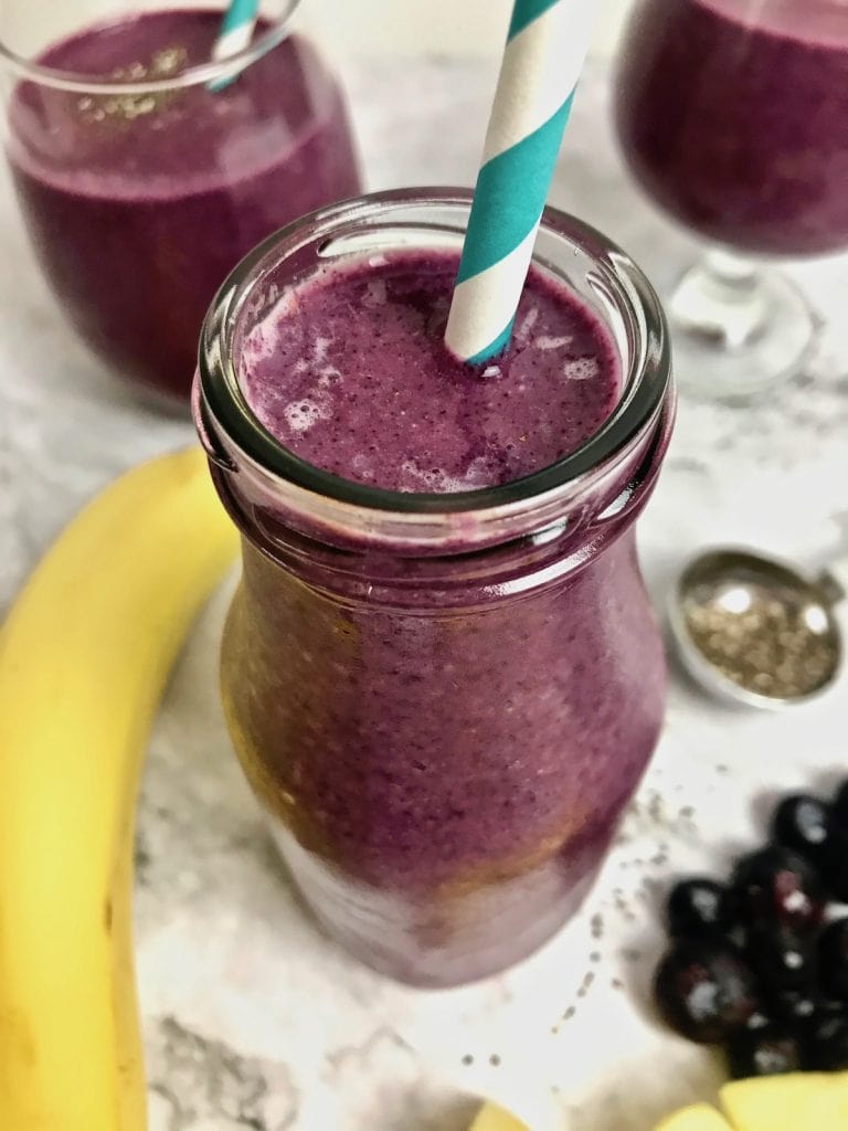 Close up of a purple blueberry pineapple smoothie with a turquoise and white striped straw. 