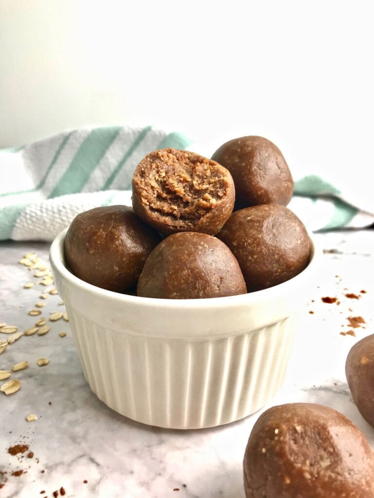 Cookie dough balls in a white bowl, with a turquoise and white striped towel in the background.