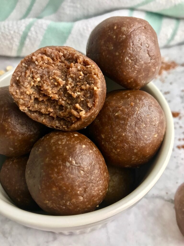 Close up of a bowl of chocolate peanut butter cookie dough balls, one with a bite taken out of it.