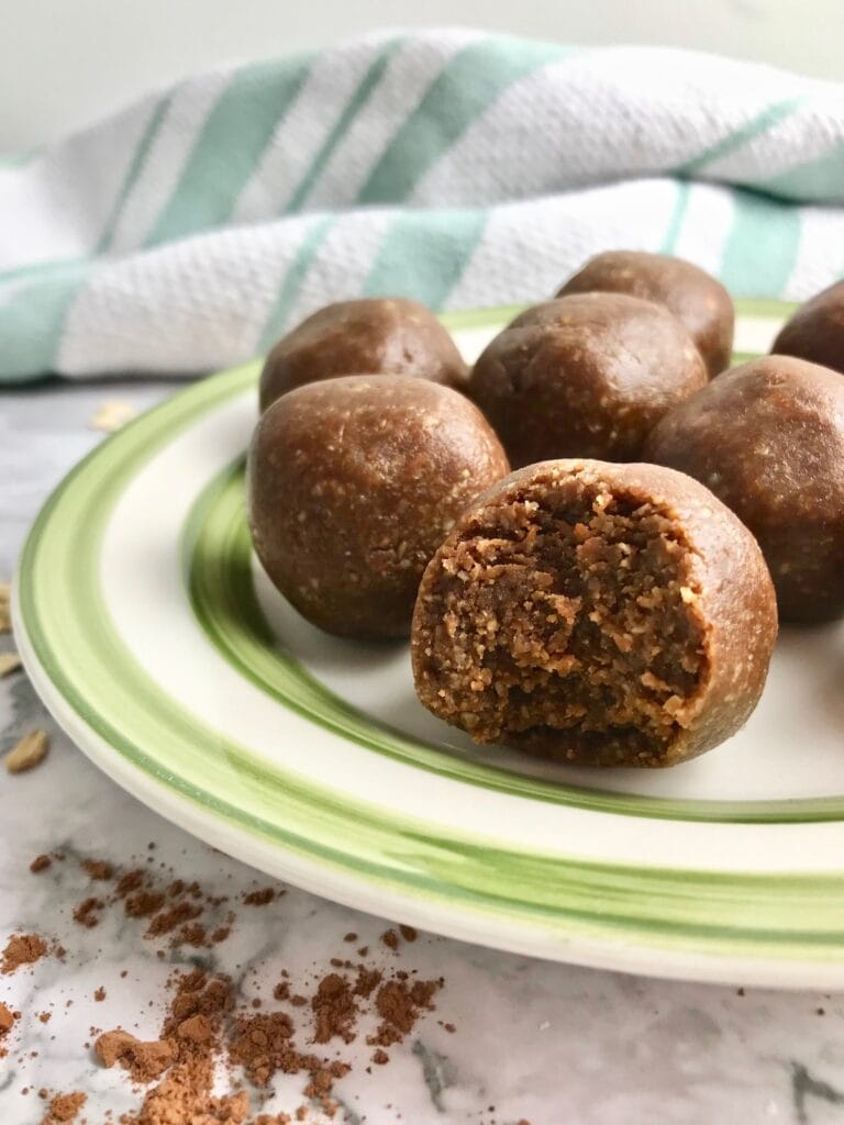 Cookie dough balls on a green and white plate with some cocoa powder on the table. 