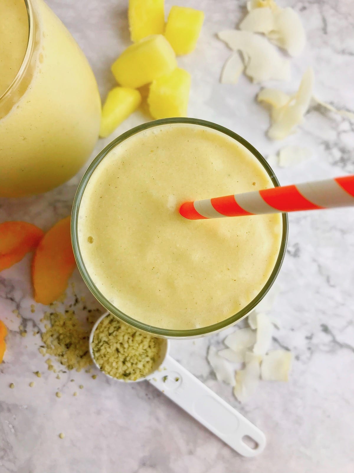 Overhead view of a yellow fruit smoothie with an orange and white straw.