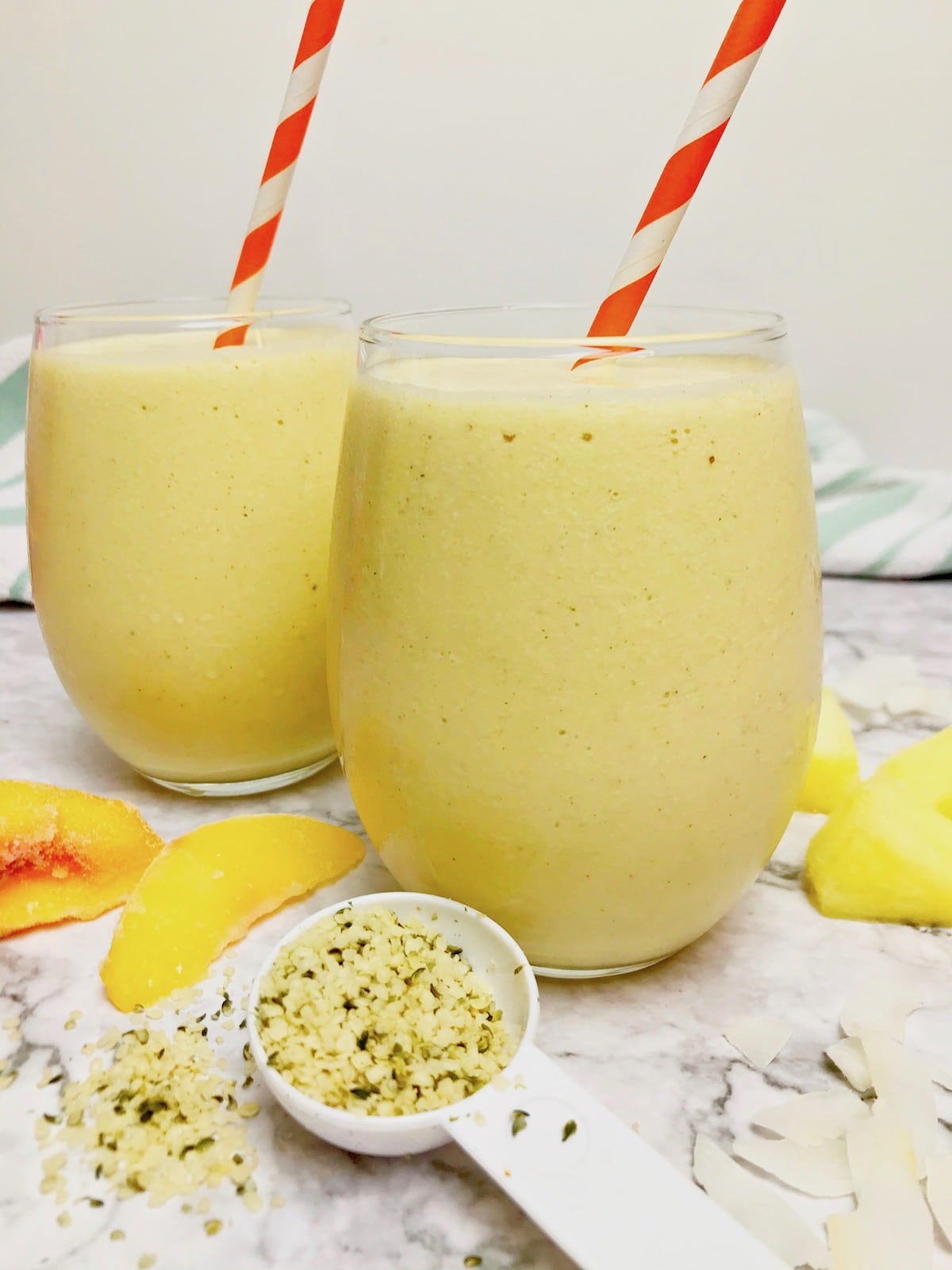 Two pineapple peach smoothies with orange and white striped straws.