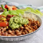 Burrito bowl with tofu, beans, guacamole, and vegetables.