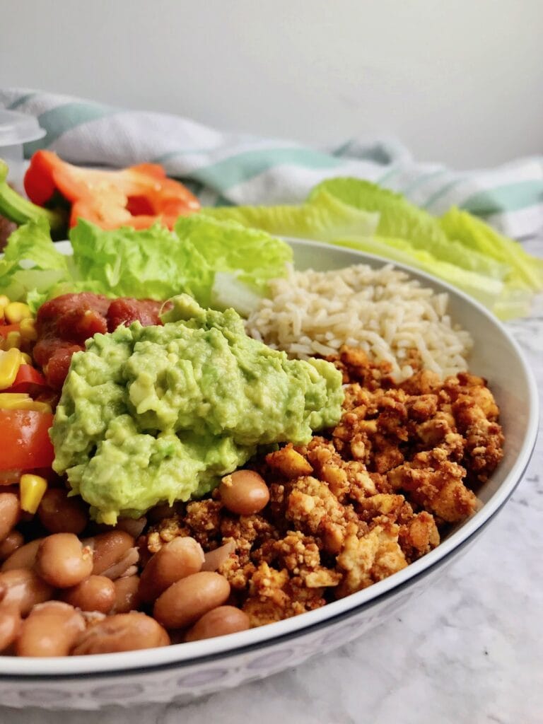 Burrito bowl closeup with beans, tofu crumble, guacamole, rice, and vegetables.