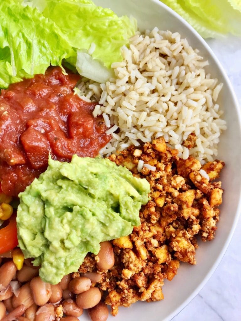 Half of a bowl, showing tofu crumble, brown rice, lettuce, salsa, guacamole, and pinto beans. 