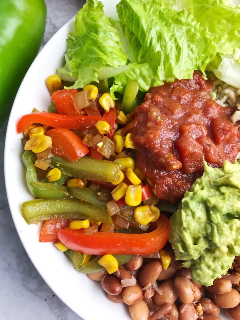 Half of a bowl showing lettuce, peppers, corn, salsa, guacamole, and pinto beans.